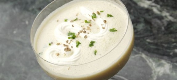 Ein cremiger Cocktail in einem Glas, garniert mit Sahne, Kräutern und Pfeffer auf einem dunklen Marmortisch.