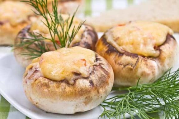 Gefüllte Champignons mit geschmolzenem Käse auf einem Teller, garniert mit frischem Dill.