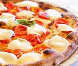 Pizza mit geschmolzenem Mozzarella, Tomatenscheiben und Basilikum auf knusprigem Rand.