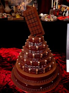 Eine Schokoladentorte mit Schriftzug '20 Ans Salon Du Chocolat' und Schokoladentafel-Dekoration.