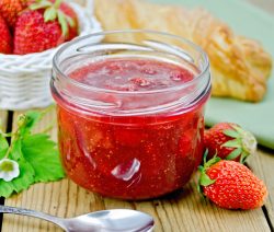 Jam of strawberry with bun and spoon on board