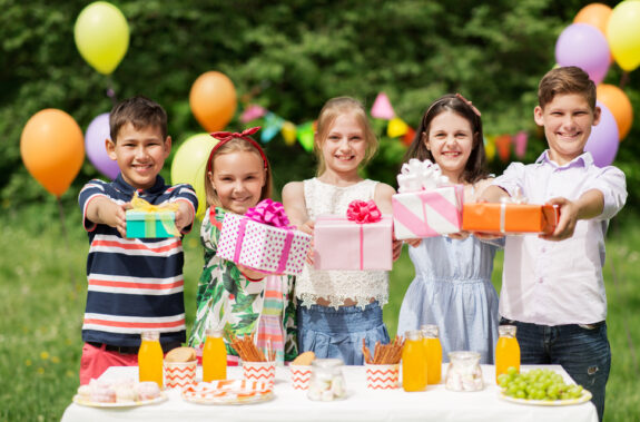 Rezepte Kindergeburtstag: Kinder stehen mit Geschenken vor Tisch