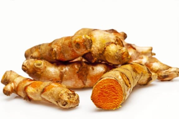Mehrere Kurkuma-Wurzeln auf weißem Hintergrund, eine angeschnitten mit leuchtend orangefarbenem Inneren.