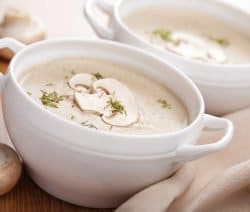 Cremige Pilzsuppe in einer weißen Schüssel, garniert mit frischen Kräutern und Pilzscheiben.