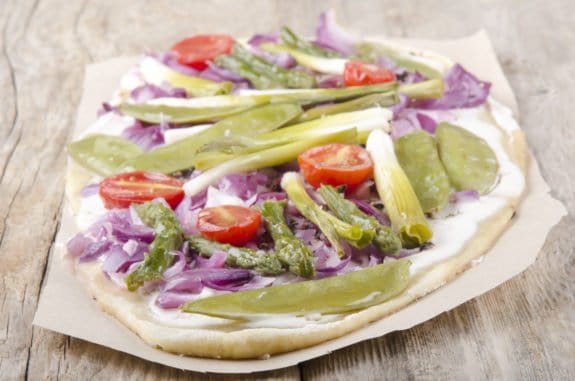 Flammkuchen mit grünem Spargel, Tomaten und Zwiebeln auf Holztisch.