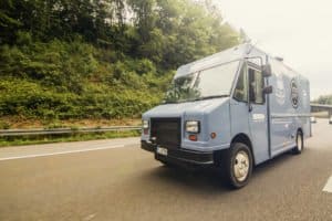 Ein blauer Lieferwagen fährt auf einer Autobahn neben grüner Vegetation.