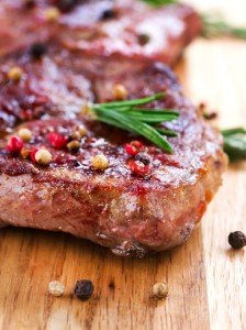 Ein gebratenes Steak auf Holzbrett, garniert mit Pfefferkörnern und Rosmarinzweig.