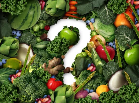 Verschiedenes Obst und Gemüse, darunter Grünkohl, Äpfel und Spargel, umrahmen ein weißes Fragezeichen.