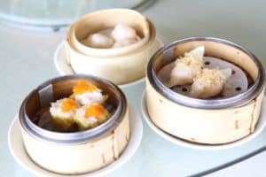 Drei Bambusdämpfer mit verschiedenen Dim-Sum-Gerichten auf einem Tisch.
