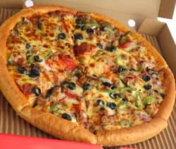 Pizza mit Oliven, Paprika und Wurst in einem offenen Pizzakarton.