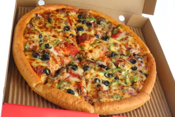 Pizza mit Oliven, Paprika und Wurst in einem offenen Pizzakarton.