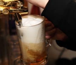 Ein Glas Bier wird aus einem goldenen Zapfhahn gezapft, Schaumkrone obenauf.