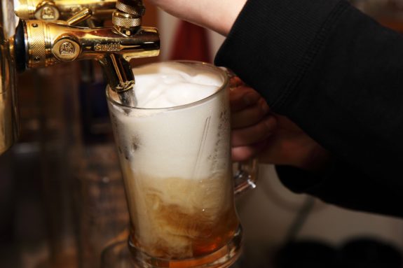 Ein Glas Bier wird aus einem goldenen Zapfhahn gezapft, Schaumkrone obenauf.