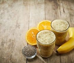 Zwei Gläser Smoothie, Banane, Orangenscheiben und Chiasamen auf Holztisch.