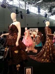Mannequins in Schokoladenkleidern auf einer Modenschau mit schwarzem Hintergrund und Scheinwerfern.