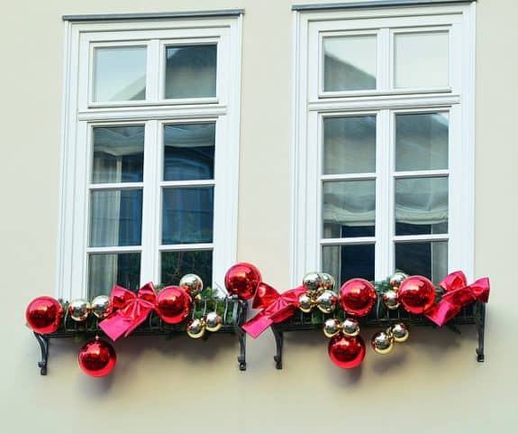 Zwei Fenster mit Weihnachtsdeko: rote und goldene Kugeln, rote Schleifen auf Fensterbänken.