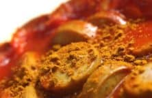 Nahaufnahme von Currywurst mit Ketchup und Currypulver aufgeschnitten.