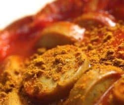 Nahaufnahme von Currywurst mit Ketchup und Currypulver aufgeschnitten.