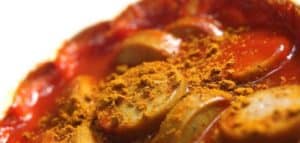 Nahaufnahme von Currywurst mit Ketchup und Currypulver aufgeschnitten.