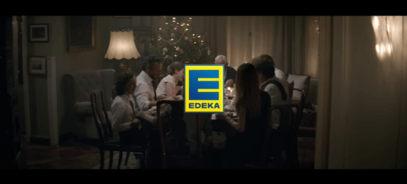 Eine Familie sitzt an einem festlich gedeckten Tisch mit Weihnachtsbaum im Hintergrund, EDEKA-Logo im Vordergrund.