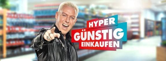 Ein Mann in Lederjacke zeigt nach vorn, daneben der Text 'Hyper günstig einkaufen' vor einem Supermarkt-Hintergrund.