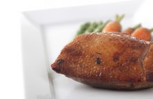 Gebratenes Entenbrustfilet auf weißem Teller, im Hintergrund Spargel und Karotten.