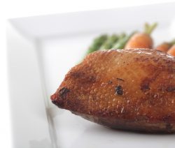 Gebratenes Entenbrustfilet auf weißem Teller, im Hintergrund Spargel und Karotten.
