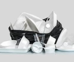 Ein schwarzer Müllsack voller Einwegplastikgeschirr und -flaschen auf grauem Hintergrund.