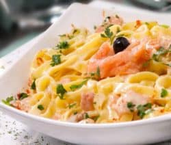 Dekorativer Teller mit Lachs Bandnudeln und einem Glas Wein im Hintergrund