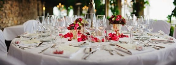 Ein elegant gedeckter Tisch mit Blumenarrangement, Weingläsern und Besteck auf weißer Tischdecke.