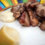 Gegrilltes Fleisch auf buntem Teller mit Zitronenspalte und Klecks Sauce.