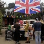 Verkaufsstand mit britischer Flagge, Menschen kaufen Pastys, Preistafel für Fleisch- und Gemüse-Pastys, bunte Wimpel.