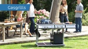 Gruppe von Menschen grillt im Garten mit einem Gasgrill, Tisch mit Getränken und Essen daneben.