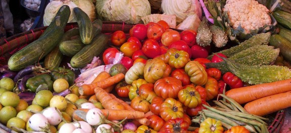 Verschiedene Gemüsesorten, darunter Tomaten, Gurken, Kohl und Karotten, auf einem Marktstand.