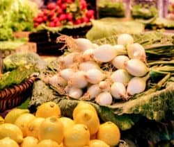 Zitronen, weiße Zwiebeln und Salat auf einem Marktstand ausgebreitet.
