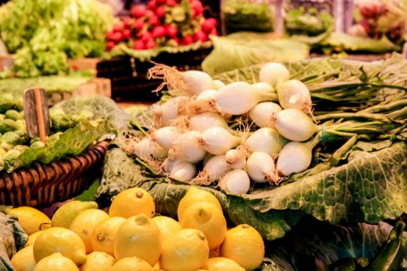 Zitronen, weiße Zwiebeln und Salat auf einem Marktstand ausgebreitet.