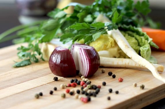 Halbe rote Zwiebel, Pfefferkörner, Petersilie und Gemüse auf einem Holzbrett.