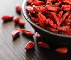 Getrocknete Goji-Beeren in einer schwarzen Schale auf einem Holztisch.