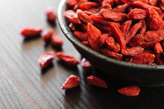 Getrocknete Goji-Beeren in einer schwarzen Schale auf einem Holztisch.