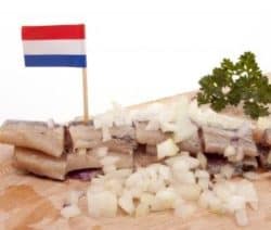 Hering mit Zwiebeln und Petersilie auf Holzbrett, niederländische Flagge steckt darin.