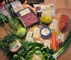 Verschiedene Lebensmittel auf einem Tisch: Gemüse, Obst, Brot, Käse und Gewürze.