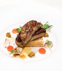 Foie gras auf Toast mit Radieschen, Gelee und Microgreens auf weißem Teller angerichtet.