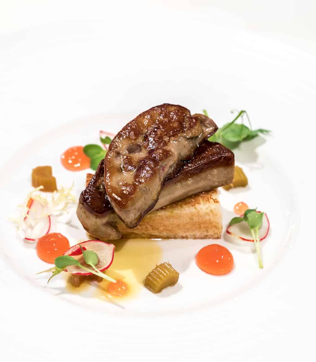 Foie gras auf Toast mit Radieschen, Gelee und Microgreens auf weißem Teller angerichtet.