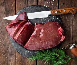 Rohe Leber auf Schieferplatte mit Messer, Pfefferkörnern und Dill auf Holztisch.
