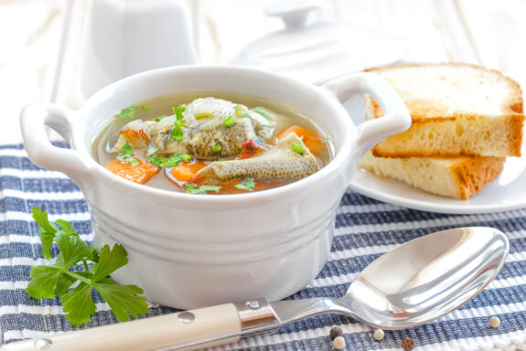 norddeutsche Fischsuppe in weißer Suppentasse mit Weißbrot im Hintergrund