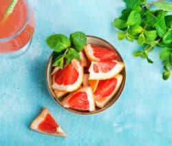Schüssel mit Grapefruitstücken und Minze, daneben ein Glas Saft und frische Minzblätter auf blauem Hintergrund.