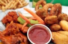 Ein Teller mit Chicken Wings, Gemüse, Zwiebelringen und Dip, im Hintergrund Pommes.
