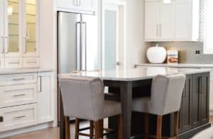 Moderne Küche mit weißem Schrank, grauer Insel, zwei gepolsterten Stühlen und Edelstahlkühlschrank.