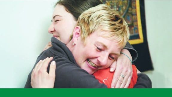 Zwei Personen umarmen sich lächelnd in einem Raum.