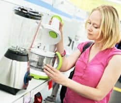 Eine Frau in rosa Bluse betrachtet eine Küchenmaschine in einem Geschäft.